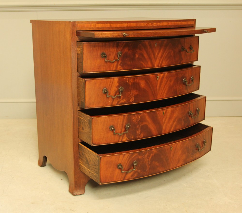 An early 20th-century mahogany bow-fronted bachelors chest of drawers featuring four graduated drawers, a top brushing slide, flame mahogany veneer, and brass handles. View VIII