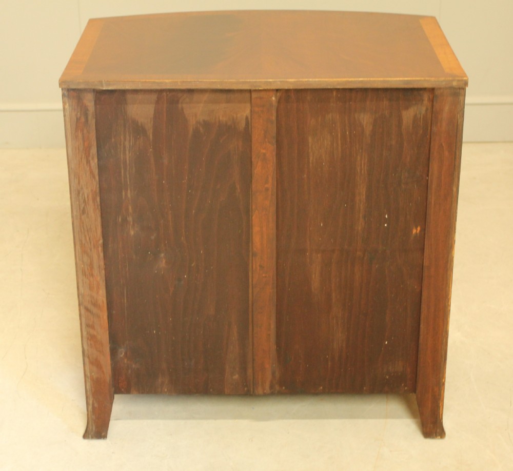 An early 20th-century mahogany bow-fronted bachelors chest of drawers featuring four graduated drawers, a top brushing slide, flame mahogany veneer, and brass handles. View XI