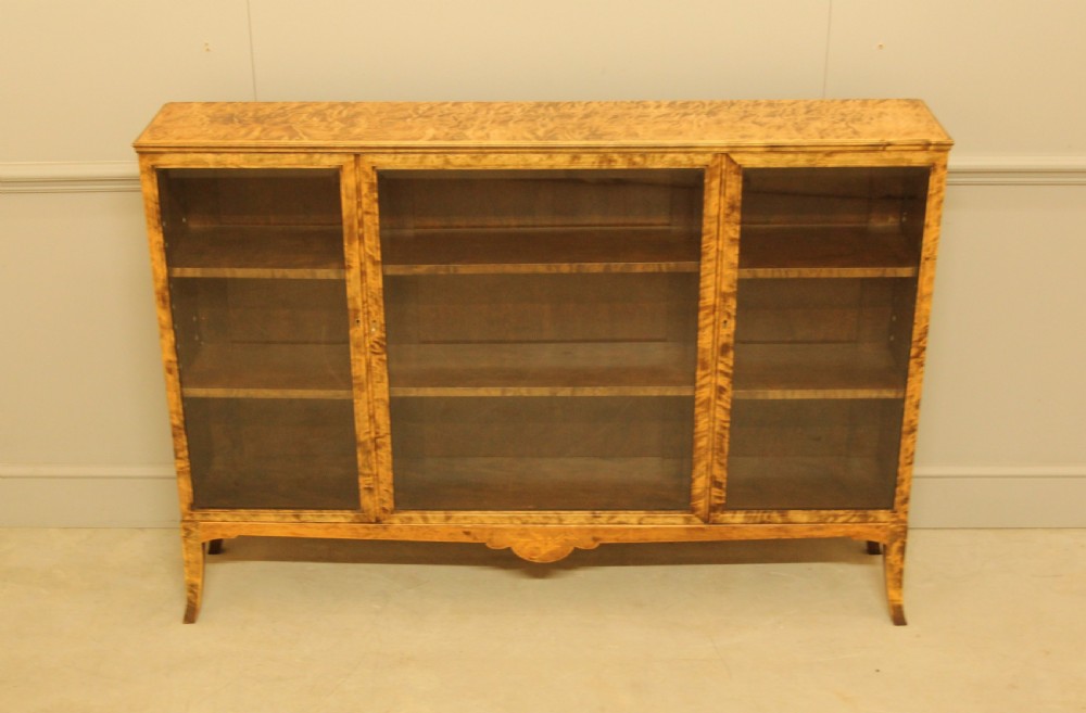 An early 20th-century Swedish low bookcase in figured satin birch veneer featuring three glazed front doors.