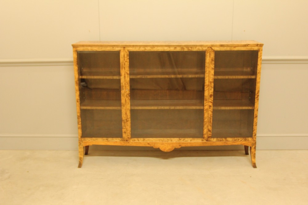 An early 20th-century Swedish low bookcase in figured satin birch veneer featuring three glazed front doors. View II