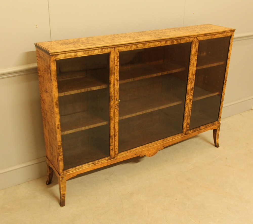 An early 20th-century Swedish low bookcase in figured satin birch veneer featuring three glazed front doors. View III