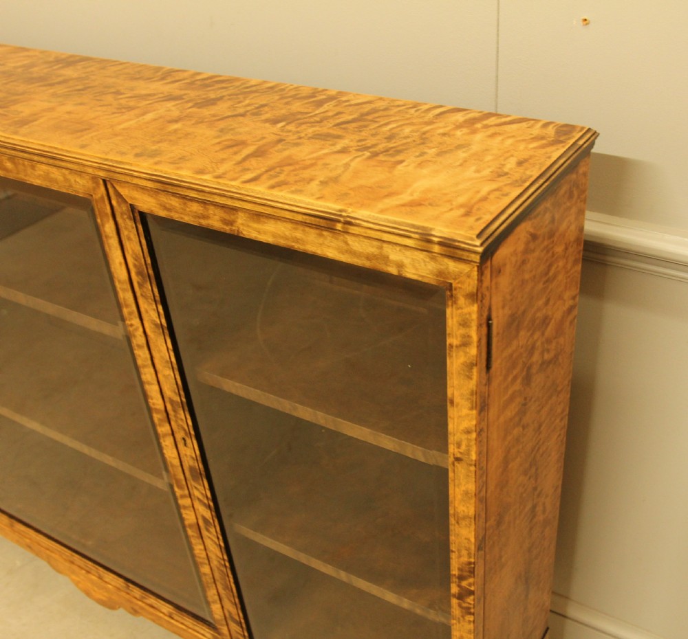 An early 20th-century Swedish low bookcase in figured satin birch veneer featuring three glazed front doors. View V