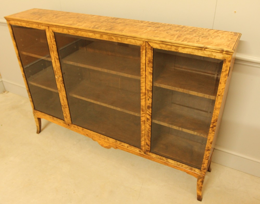 An early 20th-century Swedish low bookcase in figured satin birch veneer featuring three glazed front doors. View VI