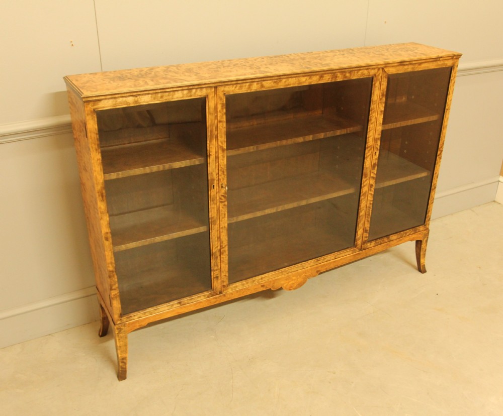 An early 20th-century Swedish low bookcase in figured satin birch veneer featuring three glazed front doors. View VII