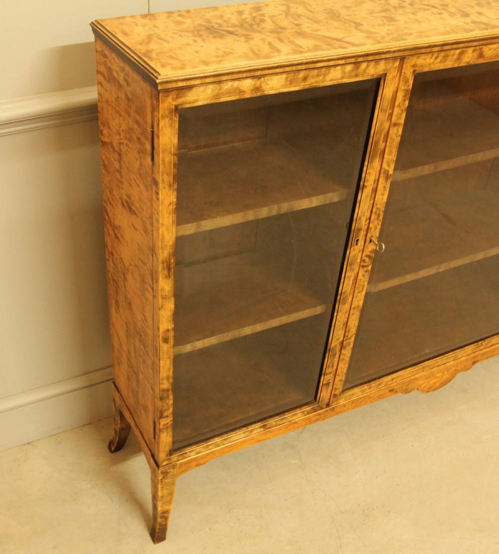An early 20th-century Swedish low bookcase in figured satin birch veneer featuring three glazed front doors. View VIII