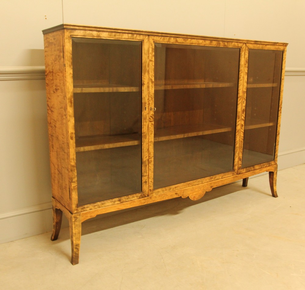 An early 20th-century Swedish low bookcase in figured satin birch veneer featuring three glazed front doors. View IX