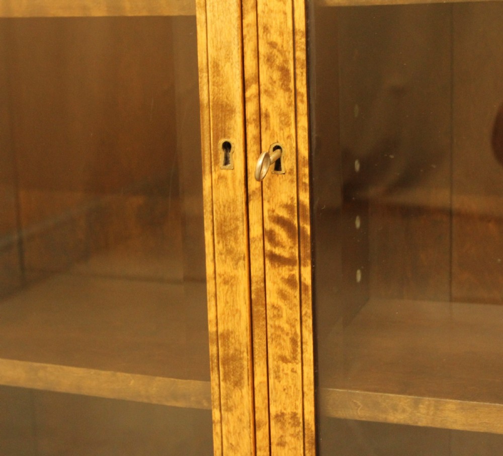 An early 20th-century Swedish low bookcase in figured satin birch veneer featuring three glazed front doors. View XI