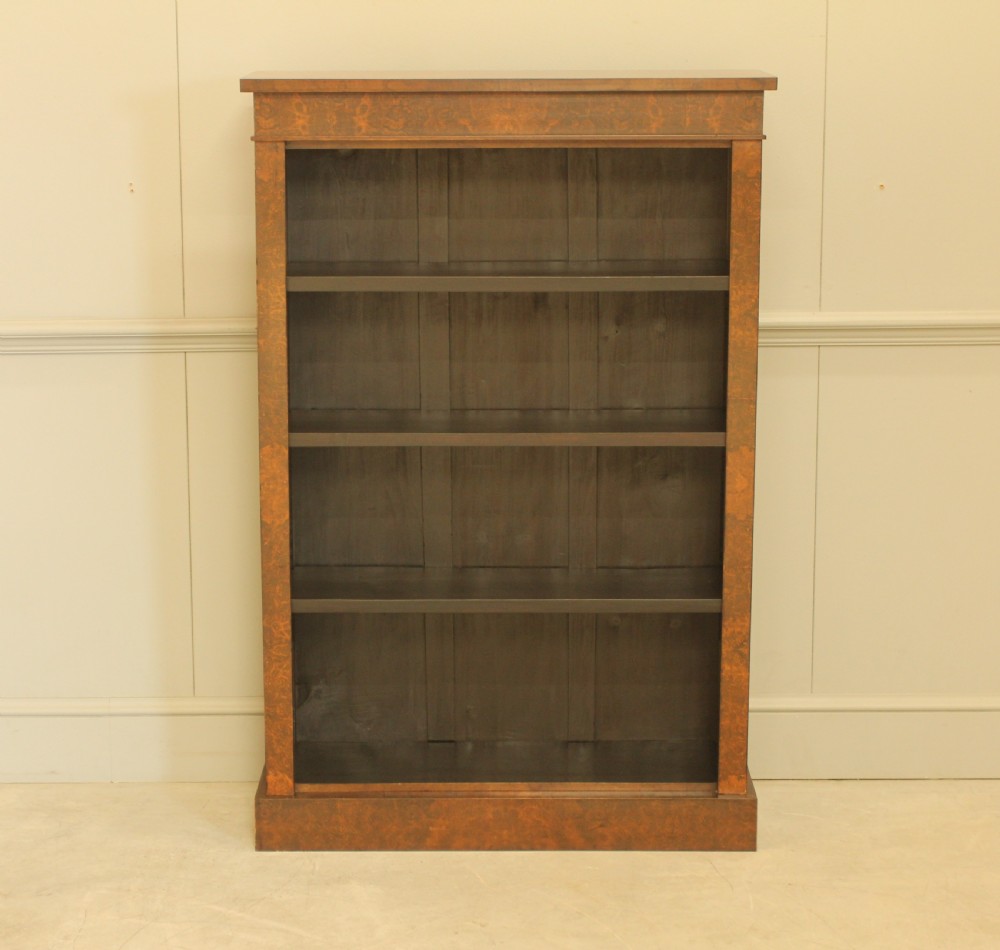A Victorian open bookcase featuring faux burr walnut outer framing, dark interior shelves, and a solid plinth base.