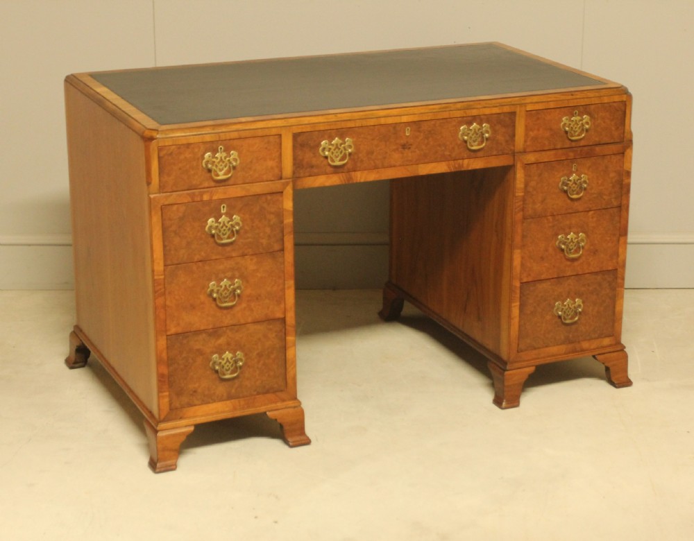 An antique burr walnut pedestal desk with a dark leather inset top, brass drop handles, and bracket feet.