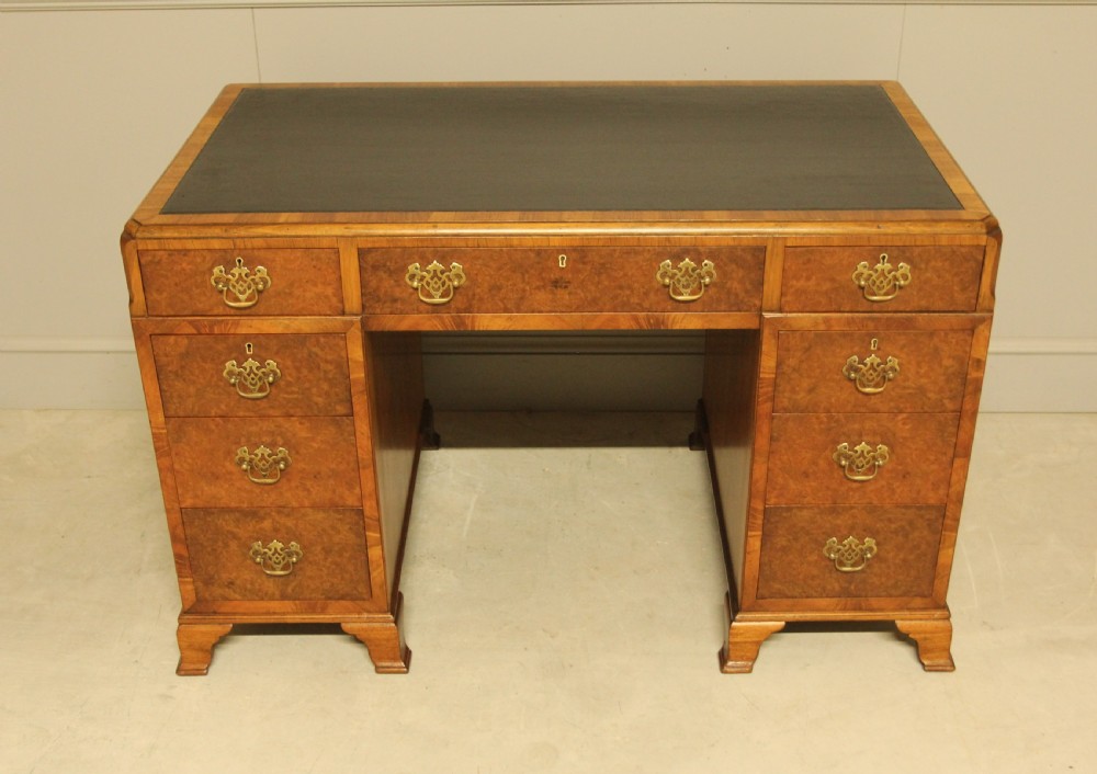 An antique burr walnut pedestal desk with a dark leather inset top, brass drop handles, and bracket feet. View VI