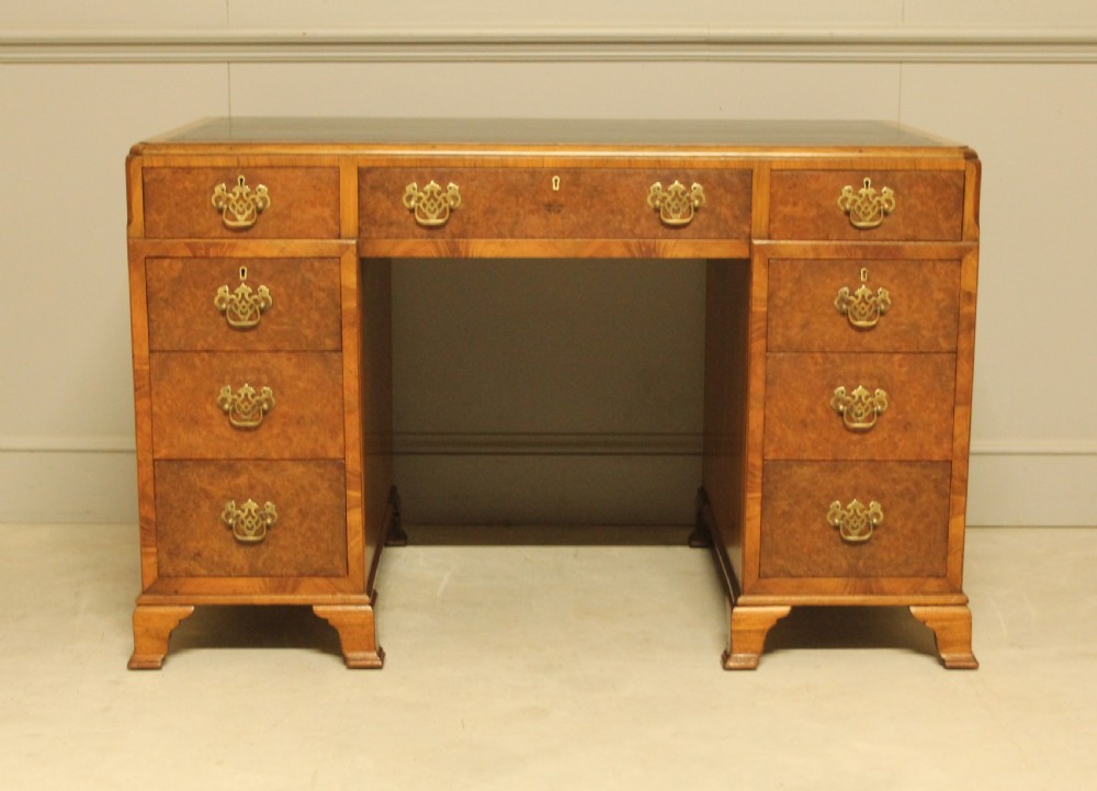 An antique burr walnut pedestal desk with a dark leather inset top, brass drop handles, and bracket feet. View VII