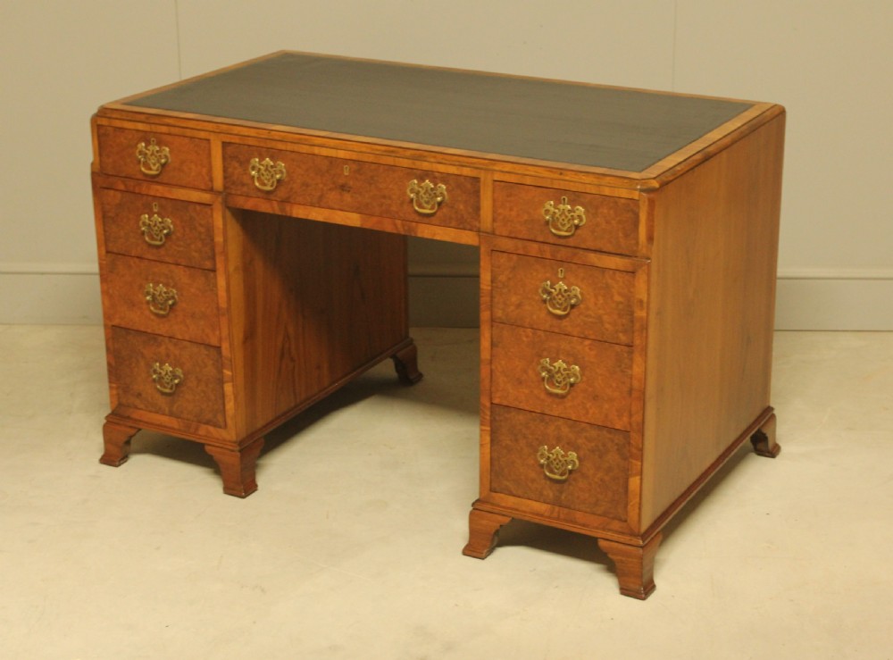 An antique burr walnut pedestal desk with a dark leather inset top, brass drop handles, and bracket feet. View VIII