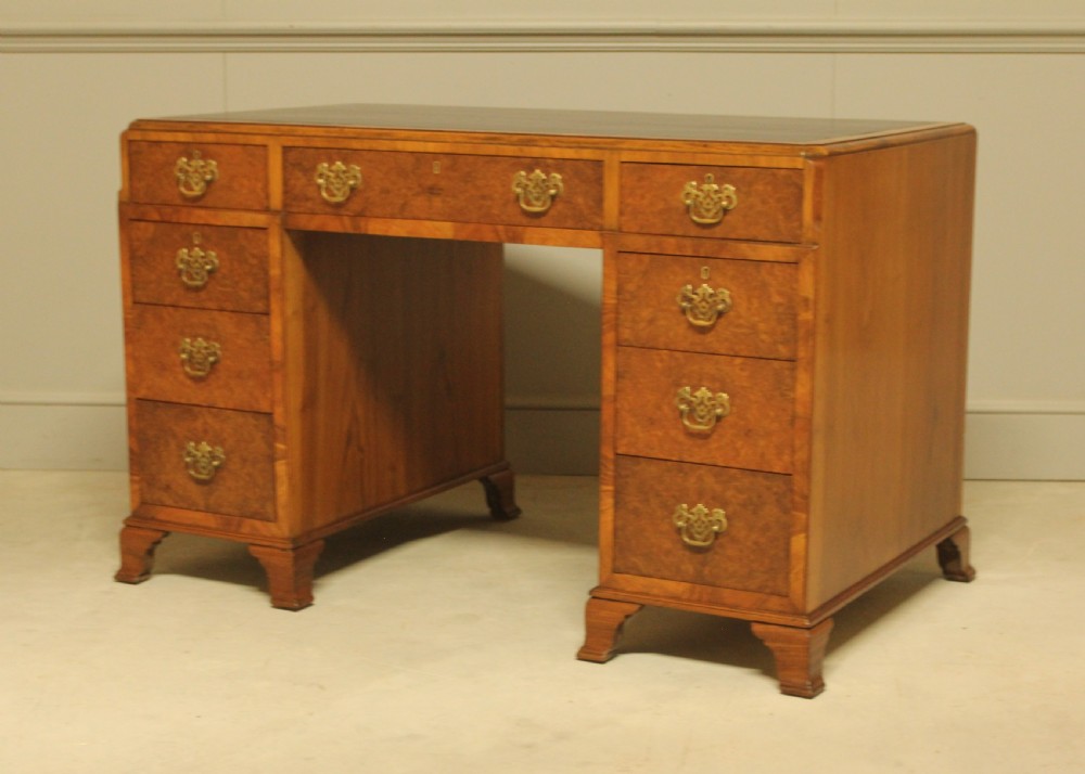 An antique burr walnut pedestal desk with a dark leather inset top, brass drop handles, and bracket feet. View IX