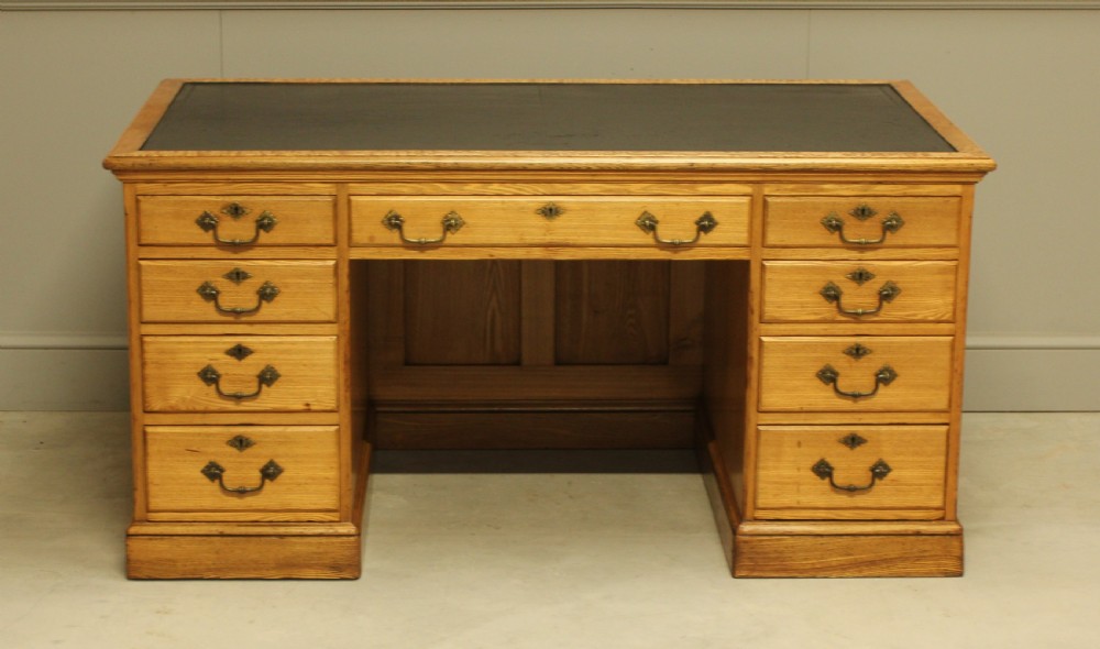 A late Victorian solid ash pedestal writing desk featuring nine drawers with brass drop handles and a dark inset top. View II