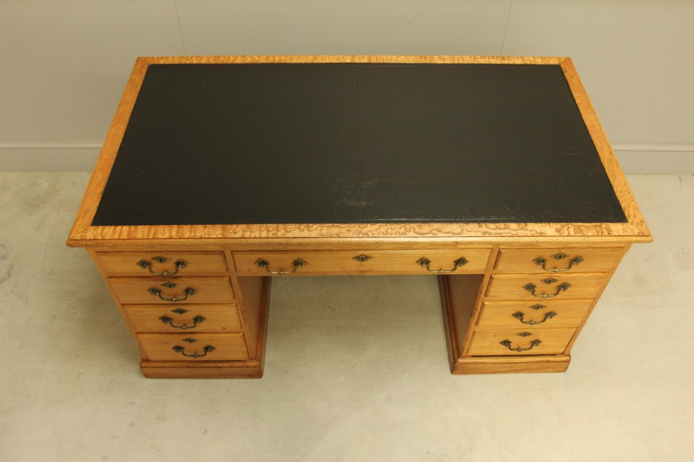 A late Victorian solid ash pedestal writing desk featuring nine drawers with brass drop handles and a dark inset top. View III