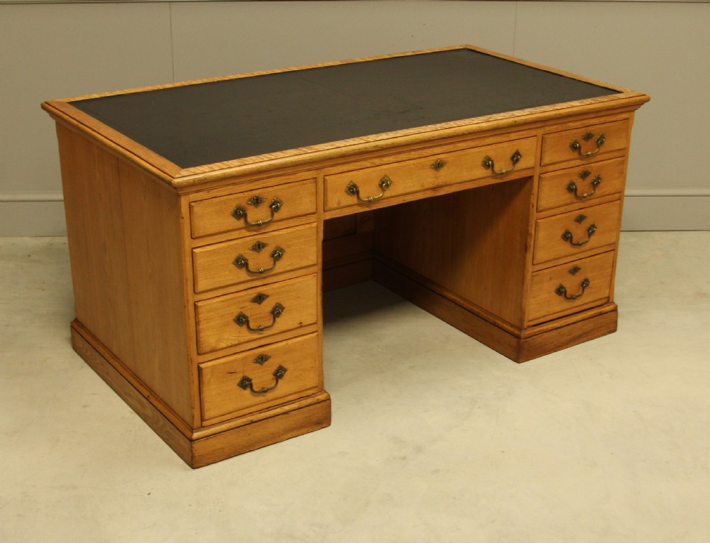 A late Victorian solid ash pedestal writing desk featuring nine drawers with brass drop handles and a dark inset top. View V