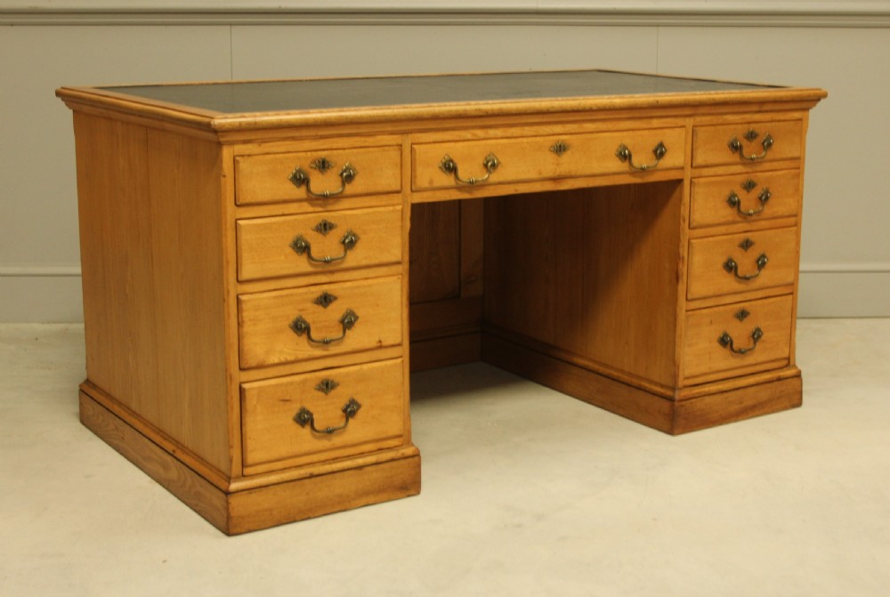 A late Victorian solid ash pedestal writing desk featuring nine drawers with brass drop handles and a dark inset top. View VI
