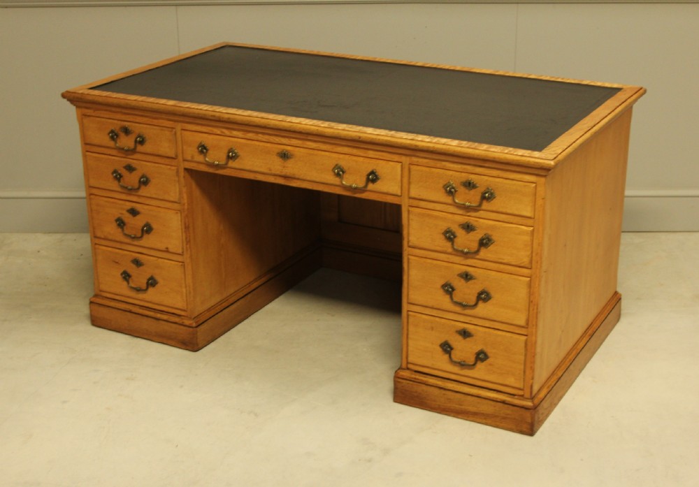 A late Victorian solid ash pedestal writing desk featuring nine drawers with brass drop handles and a dark inset top. View VII