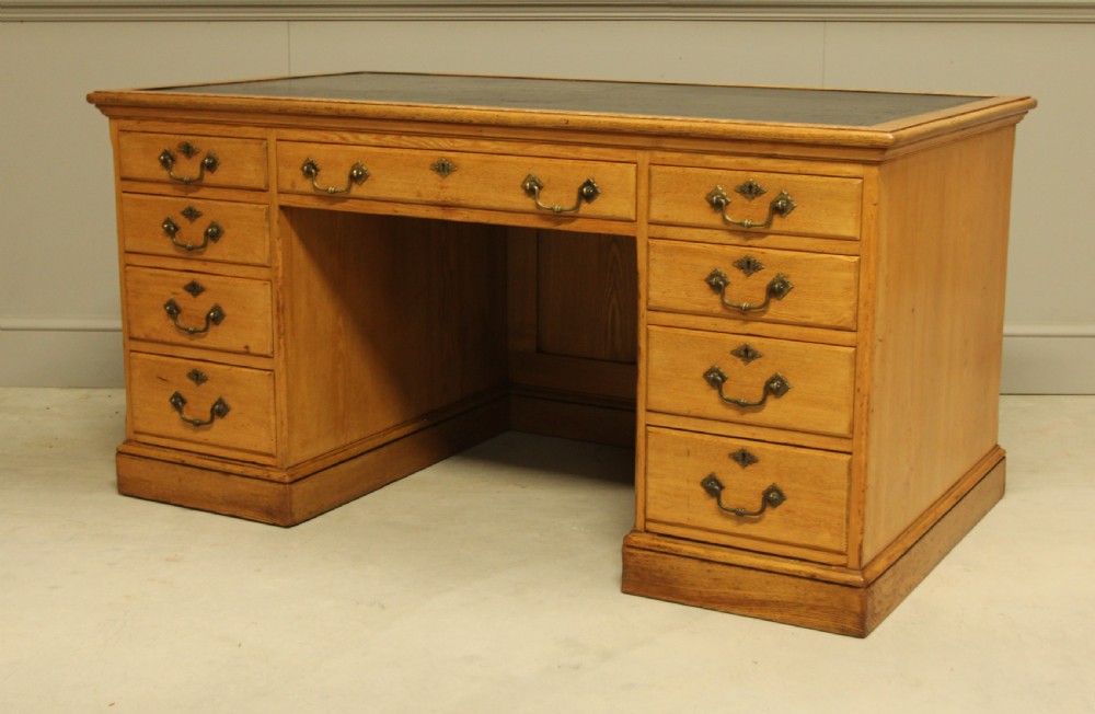 A late Victorian solid ash pedestal writing desk featuring nine drawers with brass drop handles and a dark inset top. View VIII