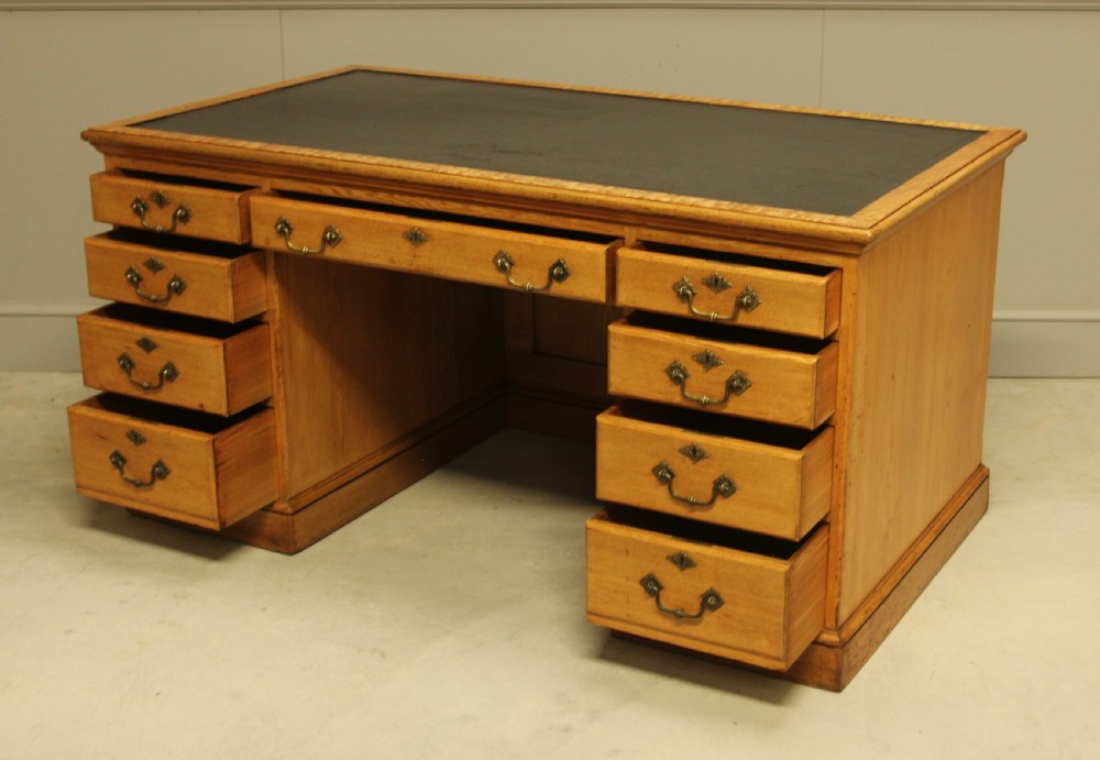 A late Victorian solid ash pedestal writing desk featuring nine drawers with brass drop handles and a dark inset top. View IX