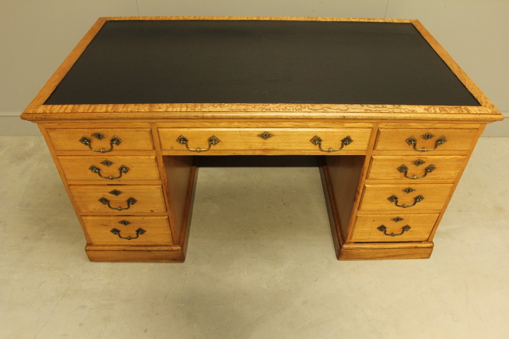 A late Victorian solid ash pedestal writing desk featuring nine drawers with brass drop handles and a dark inset top. View XI