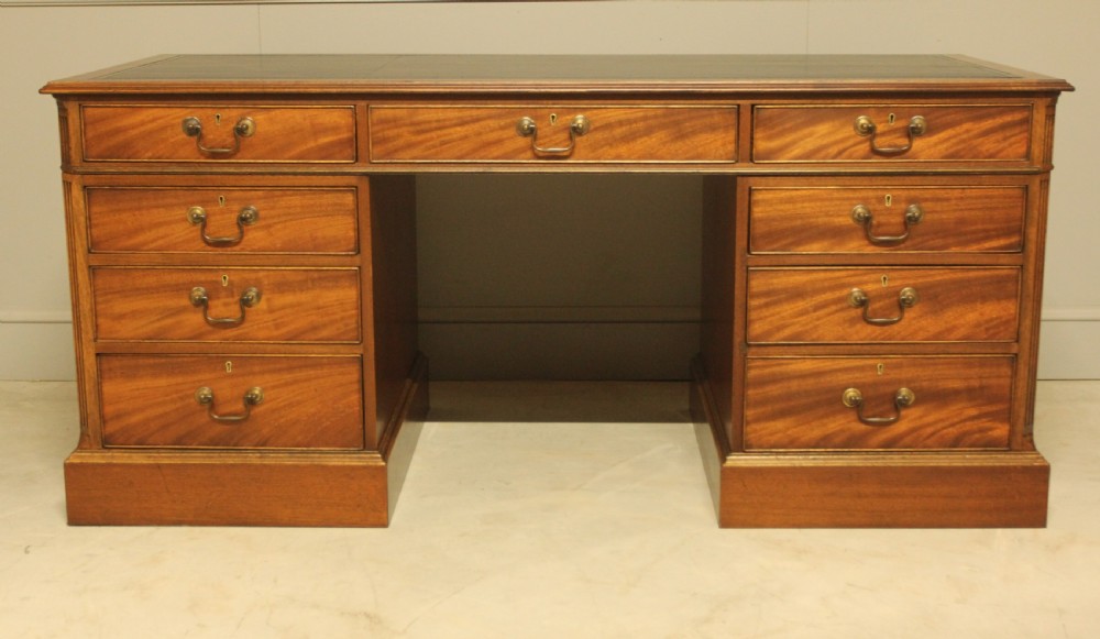 An early 20th-century twin pedestal desk crafted from curl mahogany with a dark leather inset top and brass swan-neck handles. View V