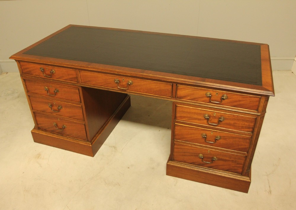 An early 20th-century twin pedestal desk crafted from curl mahogany with a dark leather inset top and brass swan-neck handles. View X