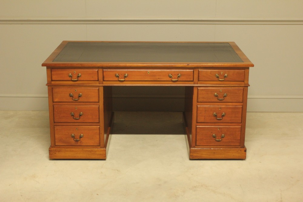 An early 20th-century mahogany pedestal writing desk featuring a dark leather inset top and nine drawers with brass swan-neck handles.