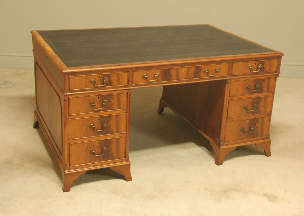An early twentieth-century curl mahogany partners desk featuring a dark leather writing top, multiple pedestal drawers with brass swan-neck handles, and bracket feet.