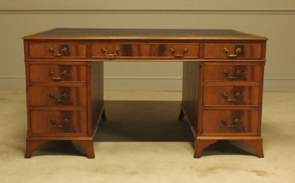An early twentieth-century curl mahogany partners desk featuring a dark leather writing top, multiple pedestal drawers with brass swan-neck handles, and bracket feet. View II
