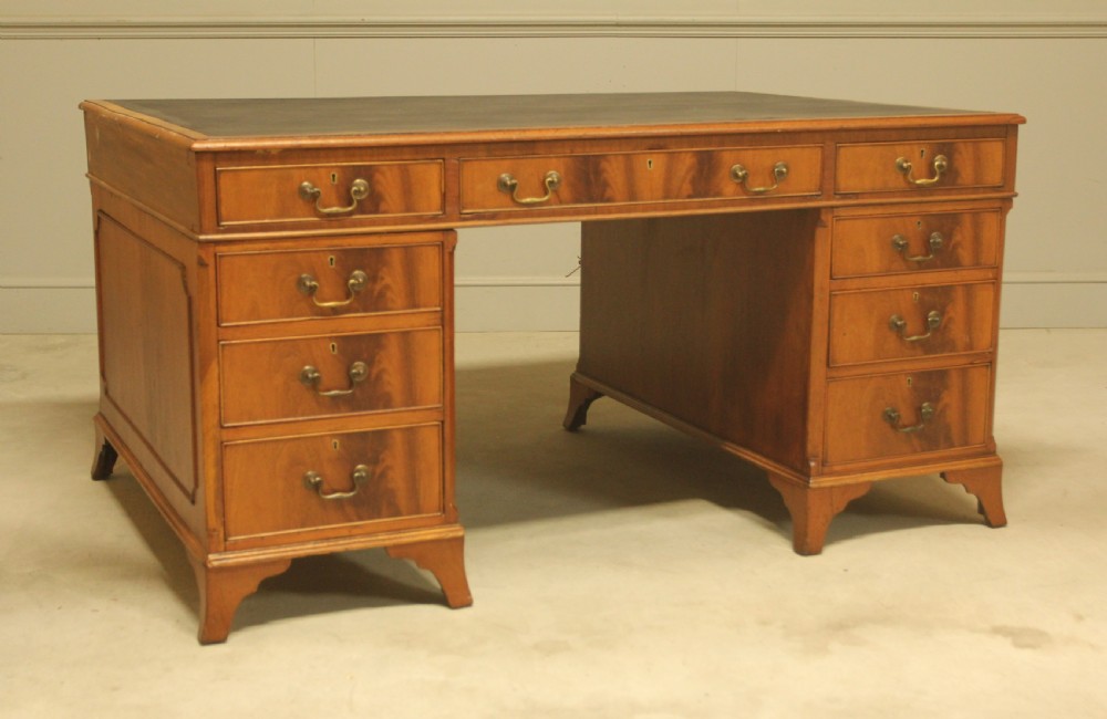 An early twentieth-century curl mahogany partners desk featuring a dark leather writing top, multiple pedestal drawers with brass swan-neck handles, and bracket feet. View IV