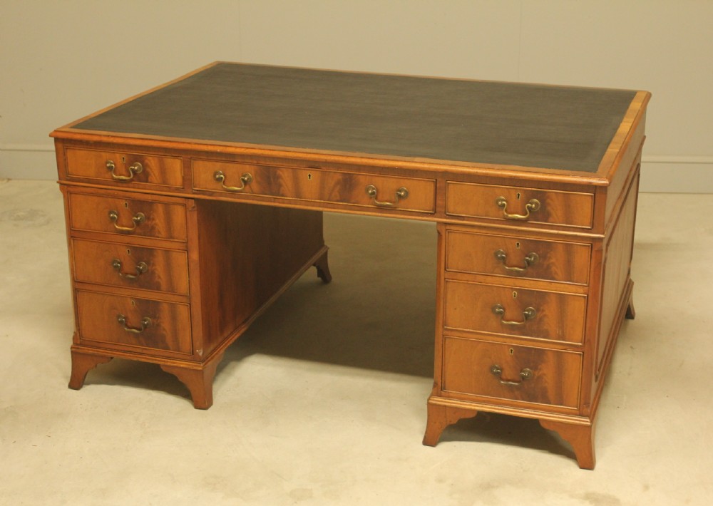 An early twentieth-century curl mahogany partners desk featuring a dark leather writing top, multiple pedestal drawers with brass swan-neck handles, and bracket feet. View V