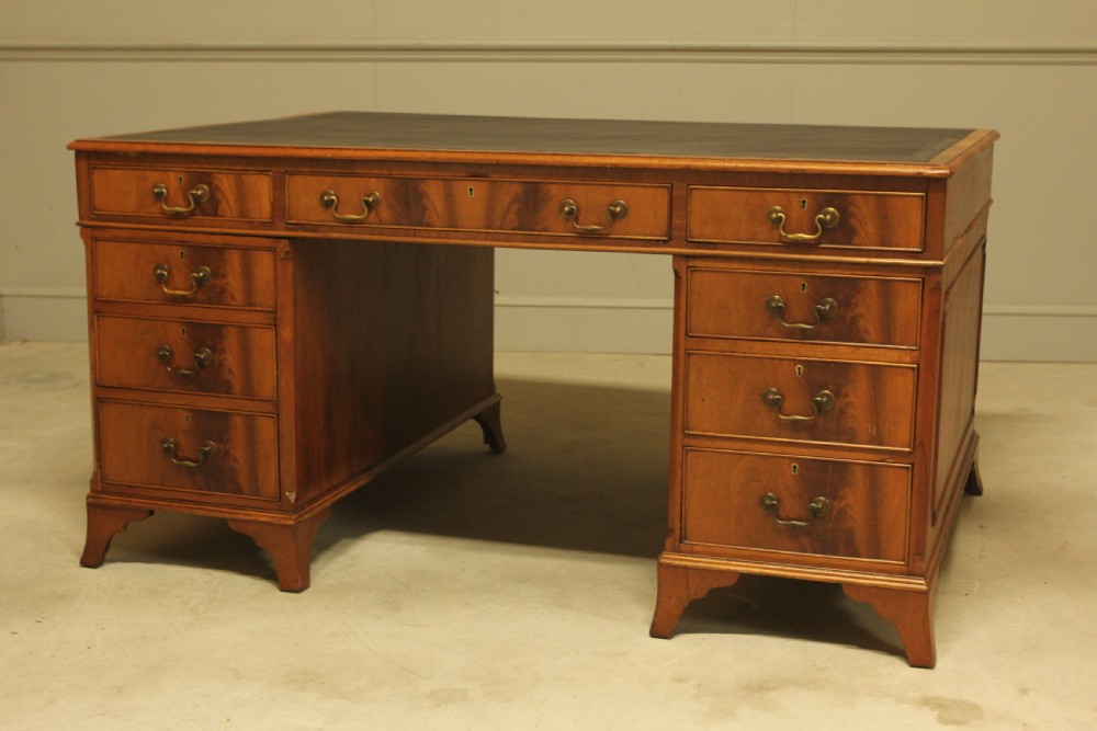 An early twentieth-century curl mahogany partners desk featuring a dark leather writing top, multiple pedestal drawers with brass swan-neck handles, and bracket feet. View VI
