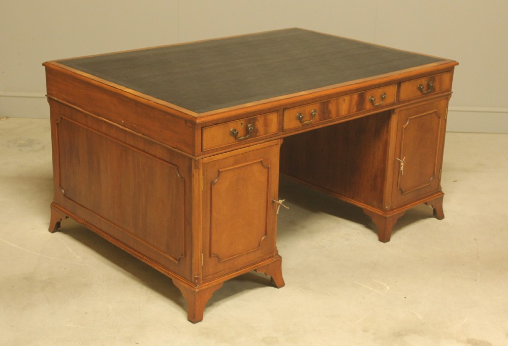 An early twentieth-century curl mahogany partners desk featuring a dark leather writing top, multiple pedestal drawers with brass swan-neck handles, and bracket feet. View VII