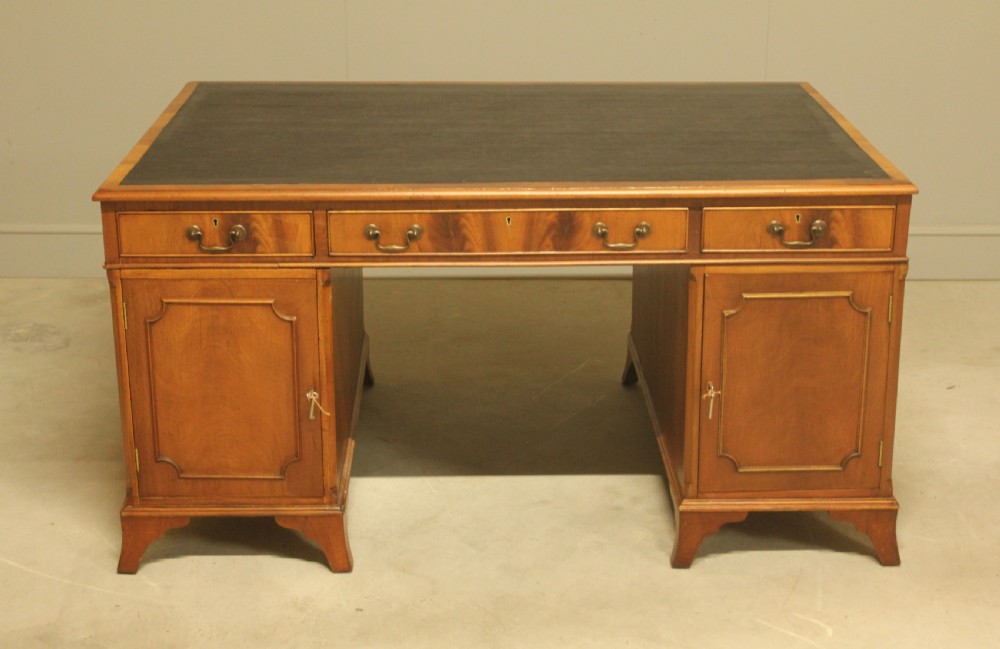 An early twentieth-century curl mahogany partners desk featuring a dark leather writing top, multiple pedestal drawers with brass swan-neck handles, and bracket feet. View VIII