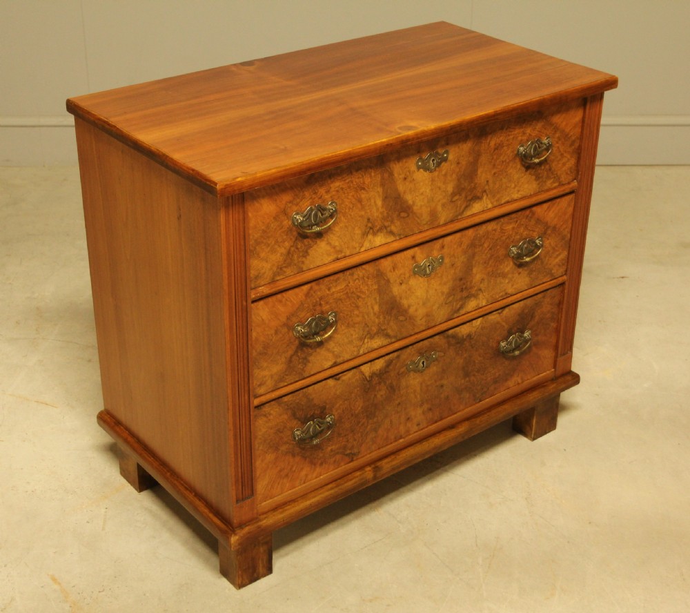An early 20th-century Swedish chest of drawers featuring three full-width drawers with rich burr walnut veneer, brass bail handles, and keyhole escutcheons. View V