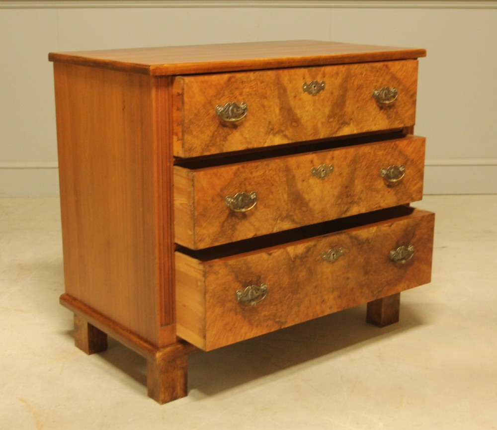 An early 20th-century Swedish chest of drawers featuring three full-width drawers with rich burr walnut veneer, brass bail handles, and keyhole escutcheons. View VI
