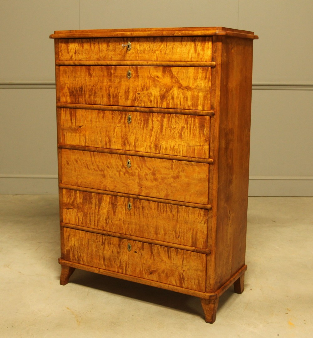 An early twentieth-century Swedish tall chest of drawers crafted in figured golden satin birch with six graduated drawers and brass escutcheons. View III