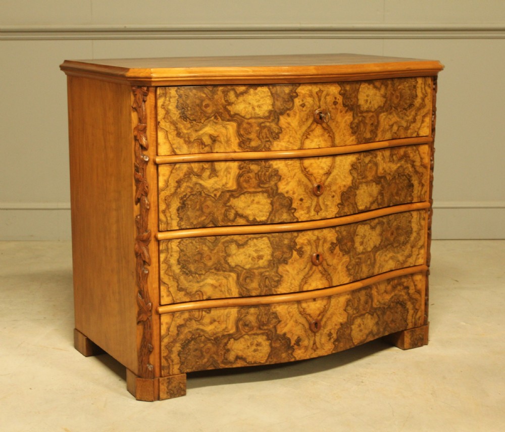 A Neo-Rococo Swedish chest of drawers featuring a serpentine front, highly figured burr walnut veneer, carved foliate corner pilasters, and four full-width drawers.