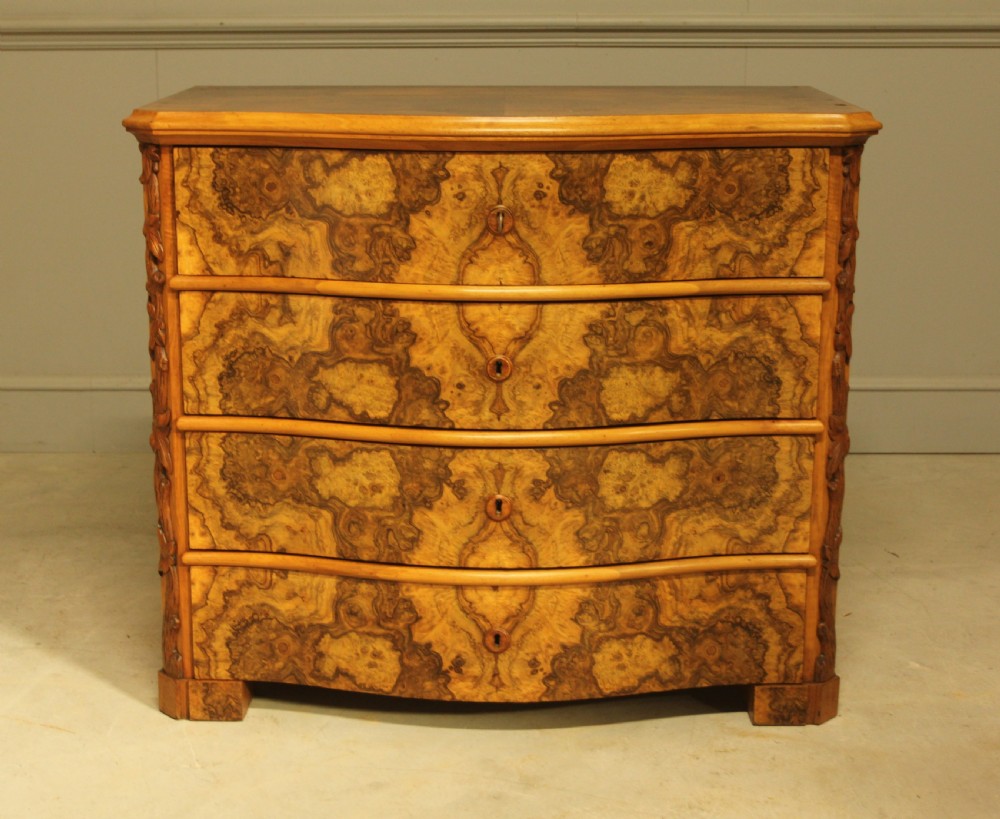 A Neo-Rococo Swedish chest of drawers featuring a serpentine front, highly figured burr walnut veneer, carved foliate corner pilasters, and four full-width drawers. View II