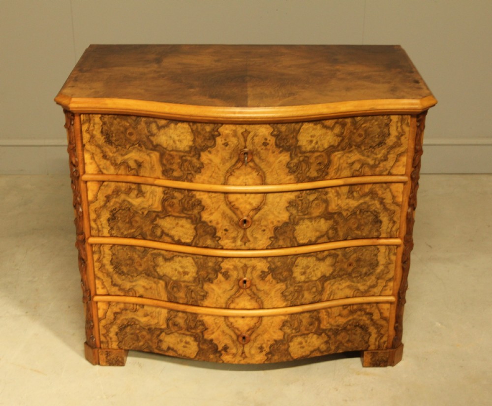 A Neo-Rococo Swedish chest of drawers featuring a serpentine front, highly figured burr walnut veneer, carved foliate corner pilasters, and four full-width drawers. View IV