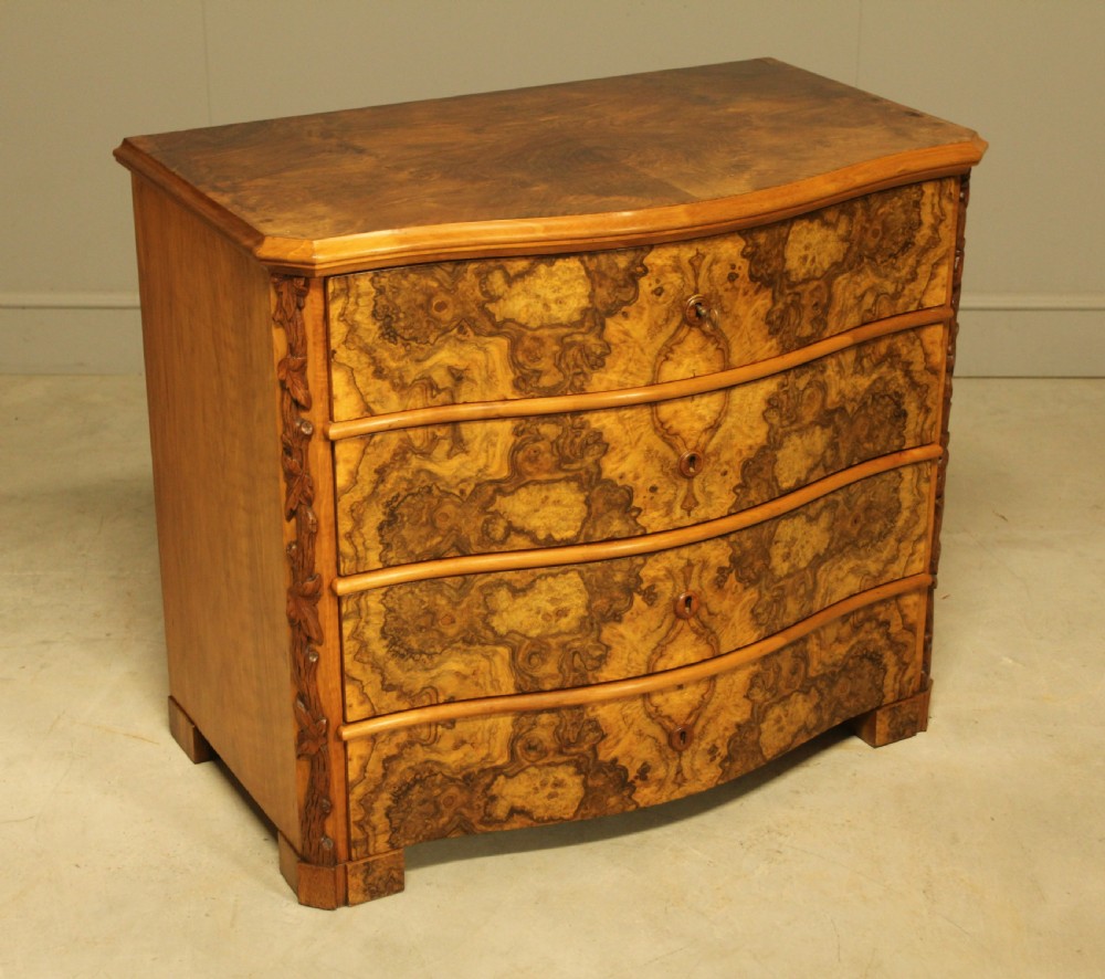 A Neo-Rococo Swedish chest of drawers featuring a serpentine front, highly figured burr walnut veneer, carved foliate corner pilasters, and four full-width drawers. View V
