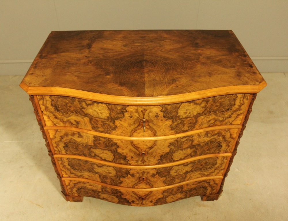 A Neo-Rococo Swedish chest of drawers featuring a serpentine front, highly figured burr walnut veneer, carved foliate corner pilasters, and four full-width drawers. View IX