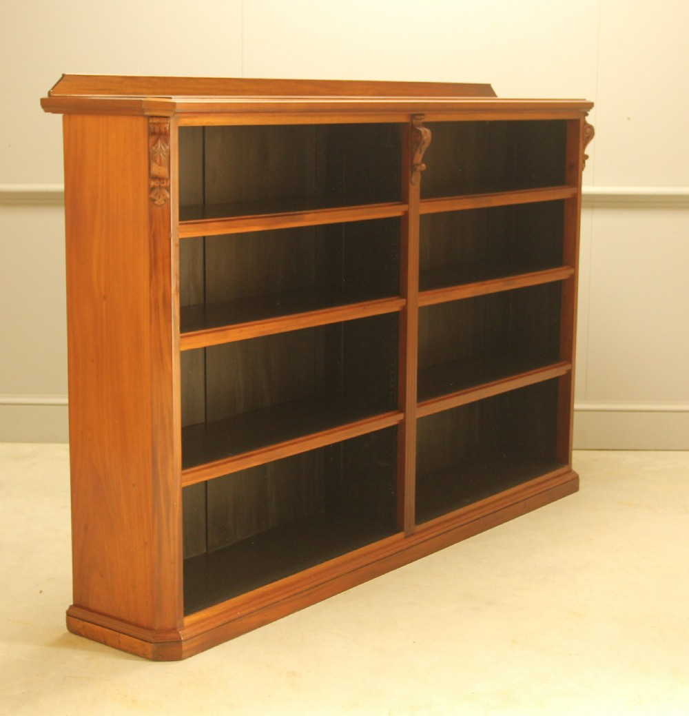 A Victorian warm brown mahogany open bookcase with two sections of shelves, carved corbel details, and a plinth base.
