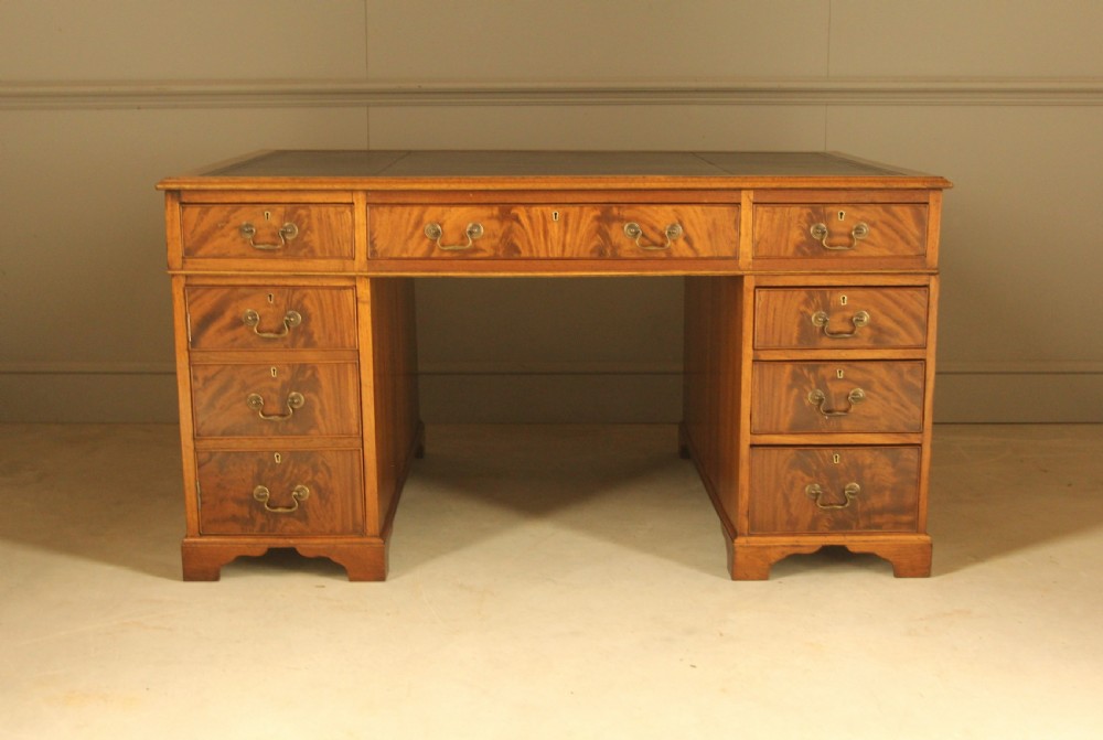 A Victorian mahogany partners desk featuring a brown leather writing inset, twin pedestals with nine drawers, and brass swan-neck handles.
