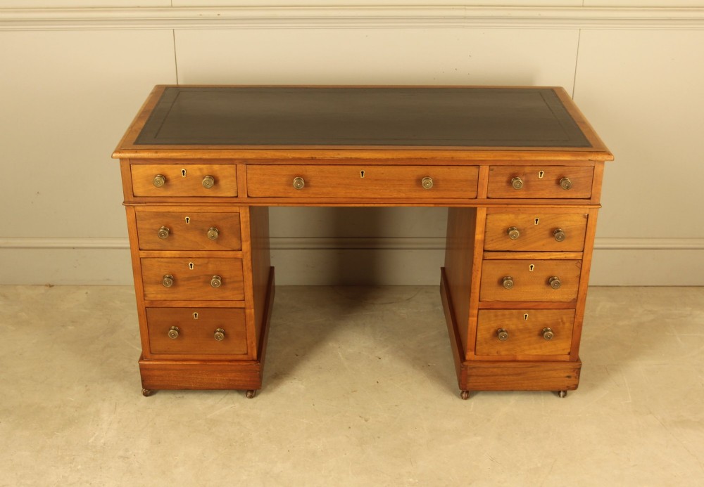 An Edwardian walnut twin-pedestal writing desk featuring nine drawers with circular brass knobs, a dark inset top, and castors mounted on plinth bases. View II