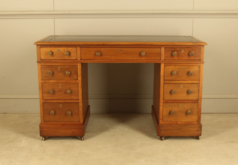 An Edwardian walnut twin-pedestal writing desk featuring nine drawers with circular brass knobs, a dark inset top, and castors mounted on plinth bases. View III