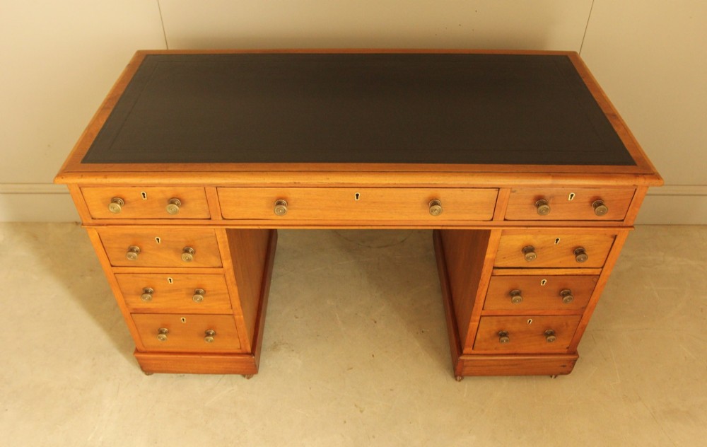 An Edwardian walnut twin-pedestal writing desk featuring nine drawers with circular brass knobs, a dark inset top, and castors mounted on plinth bases. View IV