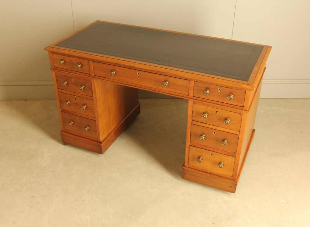 An Edwardian walnut twin-pedestal writing desk featuring nine drawers with circular brass knobs, a dark inset top, and castors mounted on plinth bases. View V