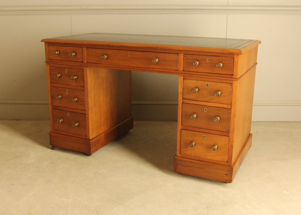 An Edwardian walnut twin-pedestal writing desk featuring nine drawers with circular brass knobs, a dark inset top, and castors mounted on plinth bases. View VI